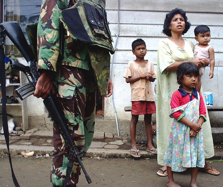 Seorang perempuan dan anak-anaknya menyaksikan seorang tentara memeriksa identitas warga setelah baku tembak antara militer Indonesia dan pemberontak separatis Gerakan Aceh Merdeka (GAM) di Aceh Besar, Aceh, 16 Agustus 2003. [AFP]