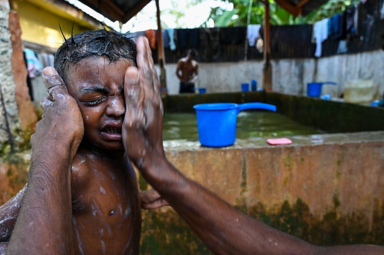 Seorang pengungsi Rohingya memandikan anaknya di penampungan sementara mereka di Padang Tiji, Kabupaten Pidie, Provinsi Aceh, pada 16 November 2023, sehari pasca kedatangan mereka dengan perahu setelah lebih dari sebulan di lautan meninggalkan Cox’s Bazar Bangladesh, tempat penampungan mereka dari persekusi junta militer di Myanmar, negara asal mereka. [Chaideer Mahyuddin/AFP]