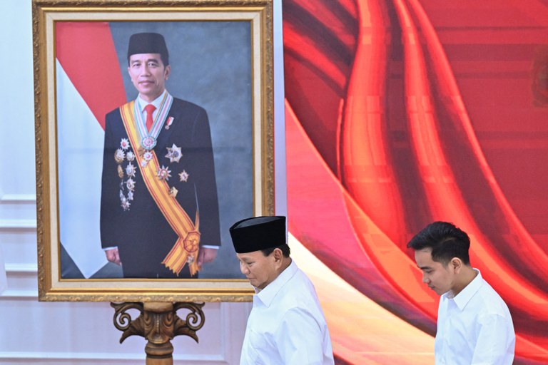 Presiden terpilih, Menteri Pertahanan Prabowo Subianto (kiri), dan wakil presiden terpilih, Wali Kota Solo Gibran Rakabuming Raka (kanan), berjalan melewati foto Presiden Indonesia Joko Widodo, ayah dari Gibran, saat rapat pleno Komisi Pemilihan Umum  yang mengumumkan hasil Pemilihan Presiden 2024 di Jakarta pada 24 April 2024. [Adek Berry/AFP]