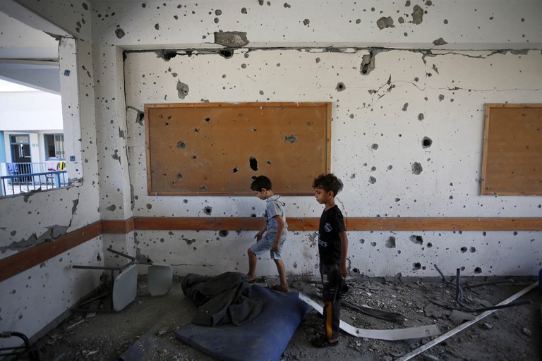Dua anak berada di ruangan yang dipenuhi lubang peluru di dalam sekolah yang dikelola PBB di kamp pengungsi Al-Maghazi di Jalur Gaza tengah, sehari setelah sedikitnya enam orang tewas dalam serangan Israel, pada 18 Oktober 2023. Puluhan orang, termasuk staf PBB terluka, kata badan PBB untuk pengungsi Palestina. [Muhammad Faiq/AFP]