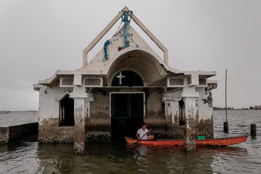 Nancy Manalaysay, seorang penjaga, mendayung keluar dari gereja yang sebagian terendam karena naiknya air laut di Sitio Pariahan, sebuah desa pesisir di Bulacan, Filipina, 26 November 2019. [Reuters]