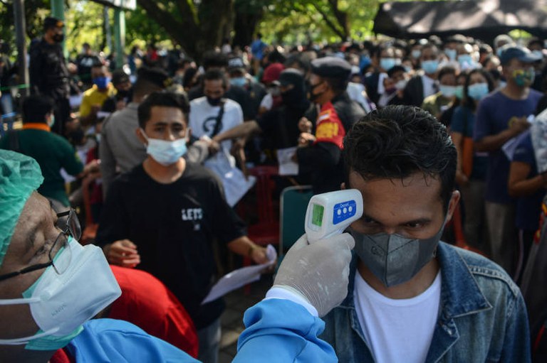 Seorang petugas kesehatan mengecek suhu salah seorang warga yang antri untuk mendapatkan vaksinasi COVID-19 AstraZeneca di Denpasar, 26 Juni 2021. [AFP]