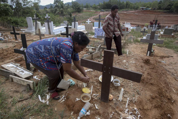 Seorang pekerja migran Indonesia meletakkan lilin di atas makam suaminya yang bekerja di perkebunan kelapa sawit di Sabah, Malaysia, 9 Desember 2018. Jenazah buruh migran yang meninggal terkadang tidak dikirim kembali ke Indonesia. (AP)