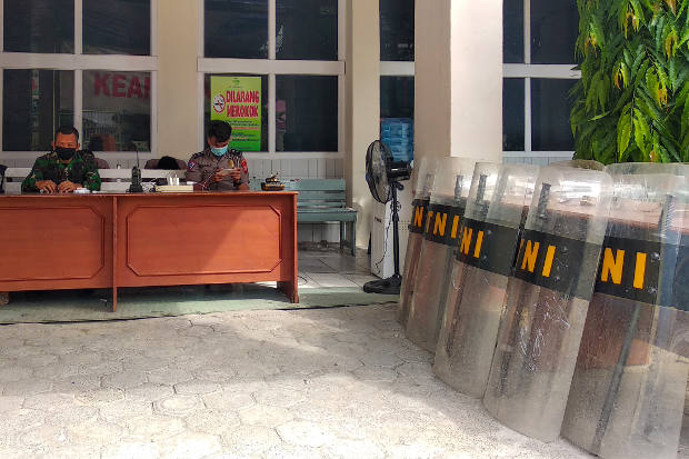 Polisi dan tentara duduk bersiaga sementara alat pelindung anti huru-hara tampak berjajar di dekat mereka di RS Stella Maris di Makassar, Sulawesi Selatan, 12 Juni 2020. Sebelumnya sejumlah anggota keluarga dari jenazah pasien COVID-19 berusaha mengambil jenazah dari sejumlah rumah sakit untuk dimakamkan oleh mereka sendiri tanpa mengikuti prosedur keamanan penanggulangan COVID-19. [AFP]