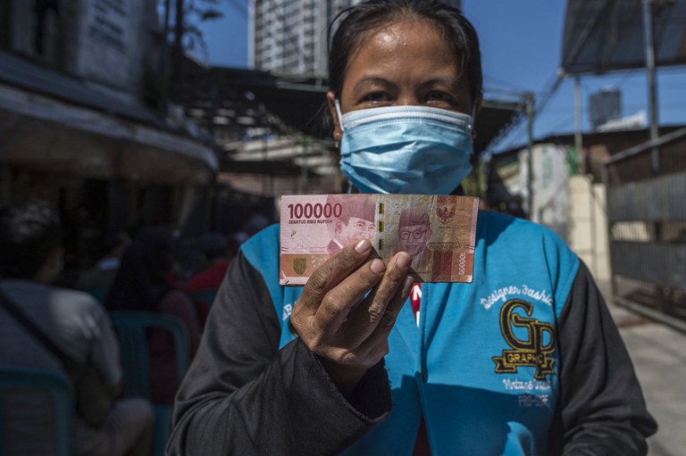 Seorang perempuan memperlihatkan uang tunai yang diberikan oleh pemerintah kepada warga yang tidak mampu secara ekonomi akibat pandemi COVID-19, di Surabaya pada 19 Juli 2021. [Foto: AFP]