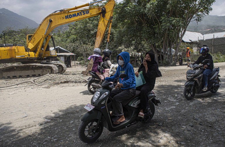 Pengendara sepeda motor menggunakan masker saat melintas di lingkar tambang galian C yang berdebu dengan alat berat di latar belakang, di Kelurahan Buluri, Palu, Sulawesi Tengah, 21 Mei 2024. [Taufan Bustan/BenarNews)