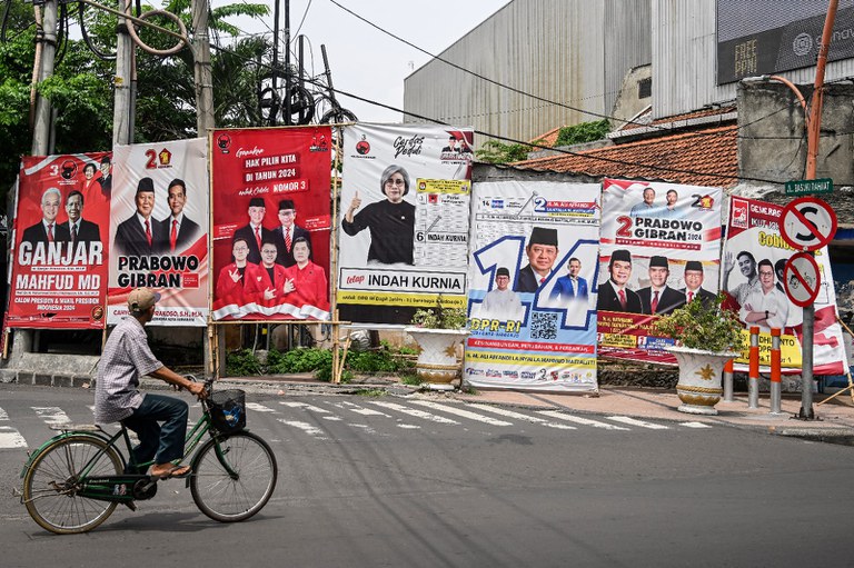 Seorang laki-laki mengendarai sepedanya melewati baliho dua pasang calon presiden-wakil presiden, serta sejumlah calon legislatif di Surabaya, 8 Januari 2024. [Juni Kriswanto/AFP]