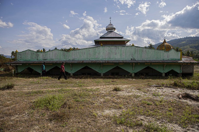 Dua warga berjalan di depan masjid Bangga yang tertimbun lumpur kering di Dusun 2, Desa Bangga, Kecamatan Dolo Selatan, Kabupaten Sigi, Sulawesi Tengah, 15 Januari 2023. Bangunan masjid yang tersisa ini rencananya tahun ini akan dirobohkan lalu didiirikan kembali oleh pemerintah desa sehingga bisa dioperasikan lagi sebagai tempat ibadah. [Taufan Bustan/BenarNews]
