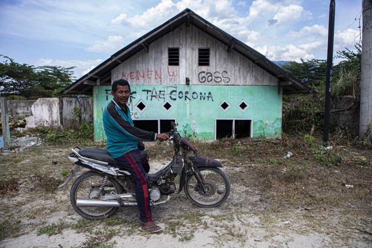 Arifin, seorang warga setempat, duduk di atas sepeda motor dengan latar belakang rumahnya yang menyisakan setengah bangunan akibat terkubur material banjir berupa lumpur bercampur pasir yang telah mengering di Dusun 2, Desa Bangga, Kecamatan Dolo Selatan, Kabupaten Sigi, Sulawesi Tengah, 15 Januari 2023. Sebanyak 590 rumah warga dengan rincian 300 rumah di Dusun 1 dan 290 rumah di Dusun 2 terkubur pasca banjir bandang yang terjadi pada 2019. Dalam musibah itu, satu korban meninggal dunia. [Taufan Bustan/BenarNews]