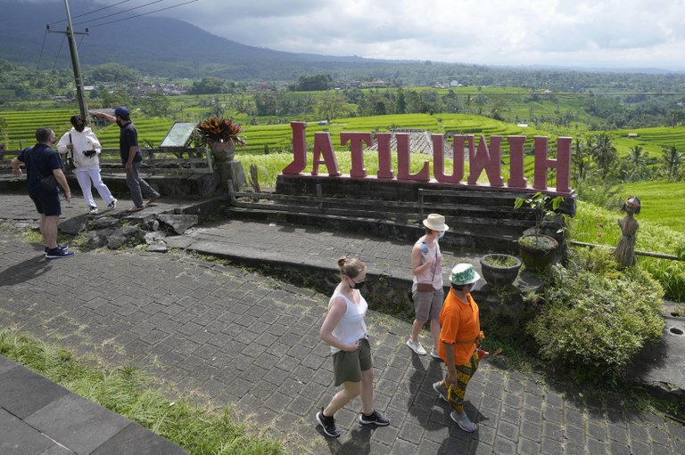 Wisatawan berjalan di dekat sawah yang diairi oleh sistem irigasi tradisional yang disebut “subak” di Bali, 18 April 2022. [Tatan Syuflana/AP]
