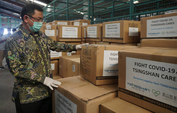 Seorang petugas mengecek paket bantuan medis dari Cina untuk membantu penanggulangan COVID-19 di Indonesia, di terminal kargo di Bandara Internasional Soekarno-Hatta, Tangerang, 27 Maret 2020. [AFP] 
