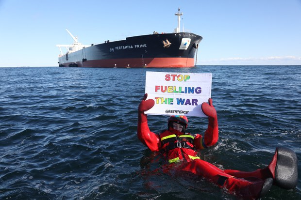 Seorang aktivis Greenpeace memegang plakat anti-perang di depan supertanker Pertamina Prime di lepas pantai Denmark pada 31 Maret 2022, mengecam pengiriman minyak Rusia yang ada dalam kapal tersebut. [Greenpeace via AFP]