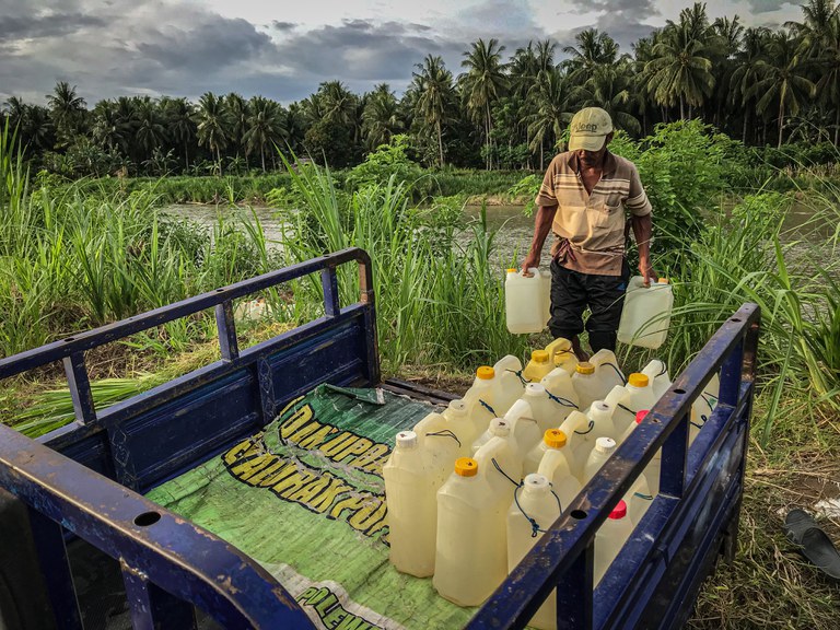 Seorang warga mengangkat jeriken berisi air bersih untuk diatur ke dalam bak sepeda motor tiga roda yang diparkir di pinggir sungai Desa Renggeang, Kecamatan Limboro, Kabupaten Polewali Mandar, Provinsi Sulawesi Barat, 11 Mei 2022. Warga menggunakan sepeda motor tiga roda agar dapat membawa banyak jeriken berisi air bersih karena untuk dijual kepada warga yang kediamannya berjarak tujuh sampai 10 kilo meter dari lokasi pengambilan air bersih. [Keisyah Aprilia/BenarNews]