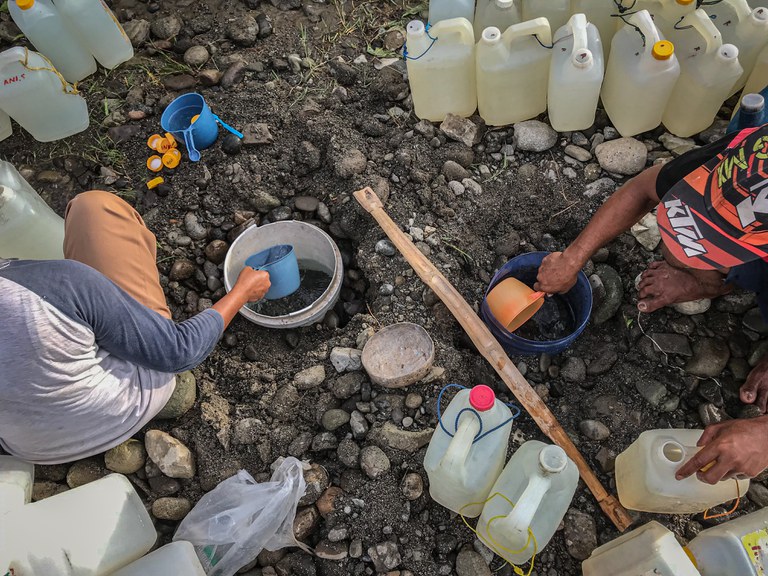 Warga mengambil air bersih menggunakan timbah plastik dari mata air di pinggir sungai Desa Renggeang, Kecamatan Limboro, Kabupaten Polewali Mandar, Provinsi Sulawesi Barat, 11 Mei 2022. Mata air ini digali sedalam 40 sampai 50 centi meter. Ketika sudah mengeluarkan air, warga menunggu 10 sampai 15 menit hingga air jernih lalu diambil lalu dimasukkan ke dalam jeriken. Uniknya, air dari mata air yang digalih di pinggir sungai ini bersih dan jernih sedangkan air di sungai keruh bercampur pasir serta lumpur. [Keisyah Aprilia/BenarNews]