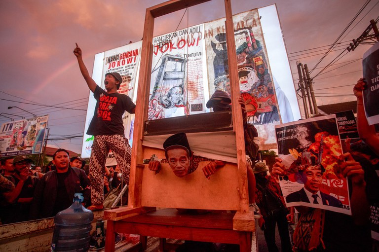 Seorang pengunjuk rasa yang mengenakan topeng Presiden Joko “Jokowi” Widodo memperagakan dirinya berada di bawah pisau guillotine dalam unjuk rasa ratusan mahasiswa menentang sepak terjang Jokowi yang dinilai tidak demokratis dan ingin mendirikan dinasti politik melalui Pemilu 2024, di Yogyakarta, 12 Februari 2024. [Devi Rahman/ AFP]
