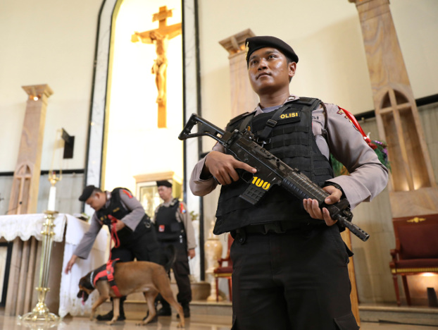 Seorang polisi berjaga-jaga ketika tim penjinak bom membawa seekor anjing pelacak saat melakukan penyisiran menjelang libur Natal di Gereja Katolik The Good Shepherd di Surabaya, Indonesia, Senin, 23 Desember 2019. [AP]