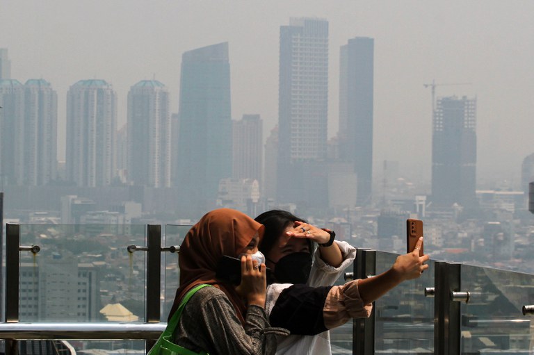Dua perempuan berswafoto di gedung tinggi dengan latar belakang langit kota Jakarta yang terlihat kelabu karena polusi udara, Kamis, 10 Agusts 2023. [Eko Siswono Toyudho/BenarNews]