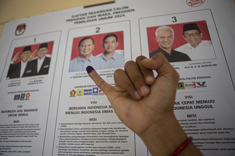 Seorang memperlihatkan jarinya yang sudah diberi tanda tinta seusai mencoblos pada Pemilu 2024 dengan latar belakang gambar para pasangan calon Anies Baswedan-Muhaimin Iskandar, Prabowo Subianto-Gibran Rakabuming Raka dan Ganjar Pranowo-Mahfud MD, di sebuah tempat pemungutan suara di Kelurahan Petobo, Kecamatan Palu Selatan, Kota Palu, Sulawesi Tengah, 14 Februari 2024. [Taufan Bustan/BenarNews]