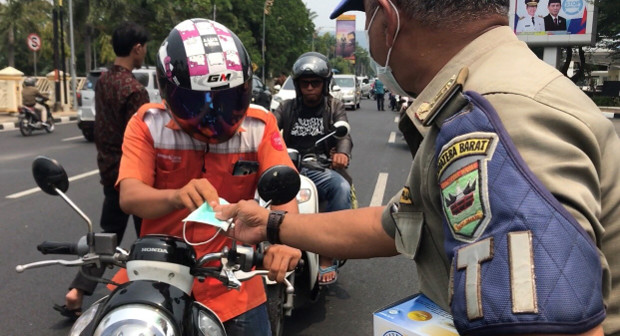 Seorang polisi membagikan masker kepada seorang pengendara sepeda motor di Padang, Sumatra Barat, 13 September 2019. (Sulthan Azzam/BeritaBenar)