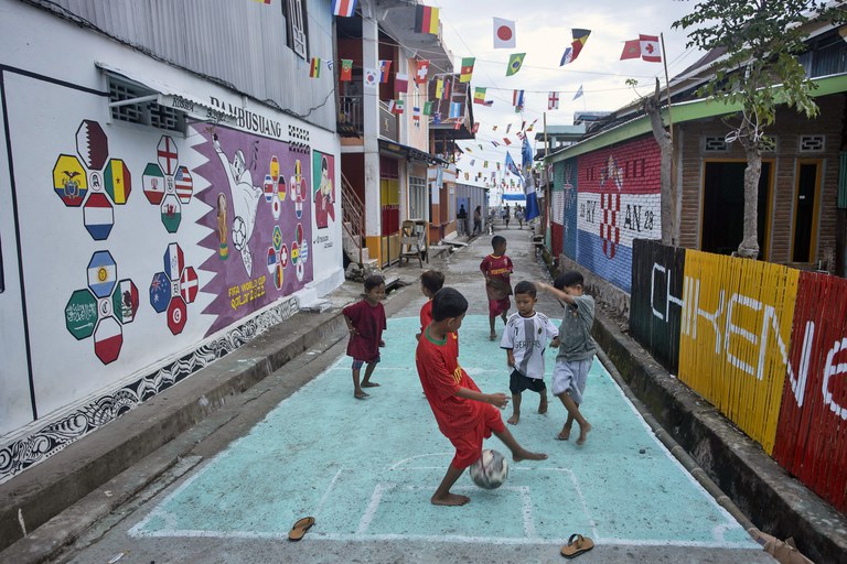Anak-anak bermain sepak bola di gang di dekat tempat tinggal mereka yang dihiasi mural bertemakan Piala Dunia 2022 di desa Pambusuang, Sulawesi Barat, 20 November 2022. [Yusuf Wahil/AP Photo]