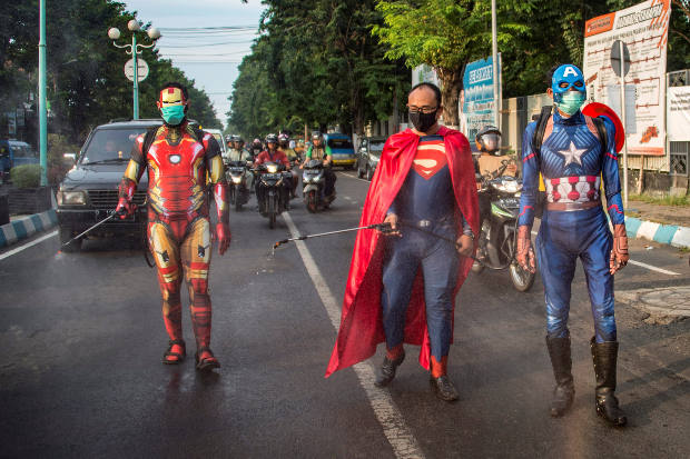 Dalam pakaian superhero, polisi di Pasuruan, Jawa Timur, melakukan disinfektan kendaraan yang lewat di salah satu jalan raya di daerah tersebut dalam upaya menanggulangi wabah COVID-19, Kamis, 9 April 2020. [AFP]