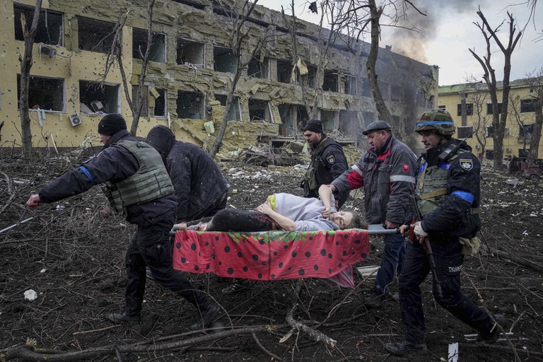 Warga Ukraina menggotong seorang perempuan hamil yang terluka keluar dari sebuah rumah sakit bersalin yang rusak akibat gempuran misil militer Rusia di Mariupol, Ukraina, 9 Maret 2022. Bayi dari perempuan itu lahir dalam keadaan meninggal. Setengah jam kemudian, sang ibu meninggal juga. [AP]