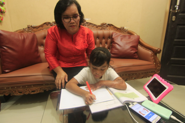 Sarina Gultom menemani putrinya, Trinity Hutahean (7), mengerjakan tugas sekolahnya, di rumahnya di Samarinda, Minggu (11/10/2020).“Saya minta Trinity menutupi kekurangan fisik dengan kemampuan akademis,” ujar sang Ibu. [BenarNews]