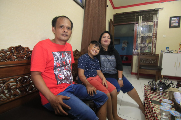 Alvaro Aurelius Tristan Sinaga (8) tampak gembira duduk diapit kedua orangtuanya di rumah mereka di Samarinda, Minggu, 11 Oktober 2020. [BenarNews]