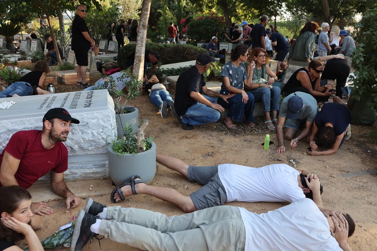 Para pelayat berlindung setelah mendengar sirene peringatan adanya serangan roket saat pemakaman seorang warga Israel yang dibunuh Hamas, dalam serangan mendadak yang dilakukan kelompok militan Palestina itu di Kibbutz Kisuffim pekan lalu, di Kibbutz Naan dekat Tel Aviv, 12 Oktober 2023. Ribuan penduduk Israel dan Palestinia tewas sejak 7 Oktober 2023 ketika Hamas melakukan serangan brutal terhadap warga sipil Israel yang memicu Israel menyatakan perang terhadap Hamas keesokan harinya. [Gil Cohen-Magen/AFP]