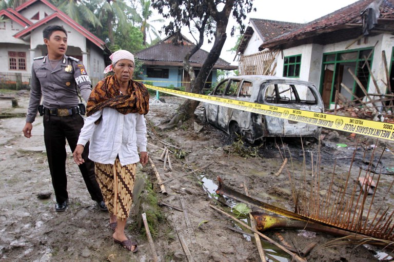 Dalam foto tertanggal 7 Februari 2011 ini, seorang polisi mendampingi Aminah, seorang pengikut Ahmadiyah, yang melihat rumahnya yang hancur di mana anaknya dan dua orang lainnya dibunuh oleh sekelompok massa yang menyerang tempat tinggal pengikut kelompok minoritas tersebut di Pandeglang, Banten. [AFP]