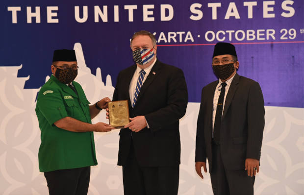 Menteri Luar Negeri AS Mike Pompeo (tengah) menerima plakat kenang-kenangan dari Ketua Umum Gerakan Pemuda Ansor, Yakut Qoumas (kiri), didampingi Sekretaris Jenderal Nahdlatul Ulama Yahya Cholil Staquf (kanan), di kantor Nahdlatul Ulama di Jakarta pada 29 Oktober 2020. (AFP)