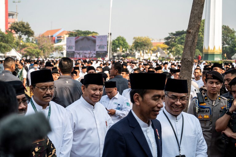 Presiden Joko Widodo (tengah) didampingi Menteri Pertahanan Prabowo Subianto (belakang), dan Ketua Pengurus Besar Nahdlatul Ulama Yahya Cholil Staquf (kanan) menghadiri peringatan Hari Santri Nasional di Surabaya, Jawa Timur pada 22 Oktober 2023, tiga hari sebelum Prabowo secara resmi mencalonkan diri sebagai kandidat presiden dalam Pemilu 2024 berdampingan dengan Gibran Rakabuming Raka, putra Jokowi sebagai calon wakilnya. [Juni Kriswanto/AFP]