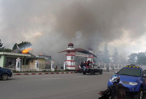 Warga berkendara melewati gedung pemerintah yang terbakar saat protes yang berubah menjadi kerusuhan di Wamena, Provinsi Papua, 23 September 2019. (AP)