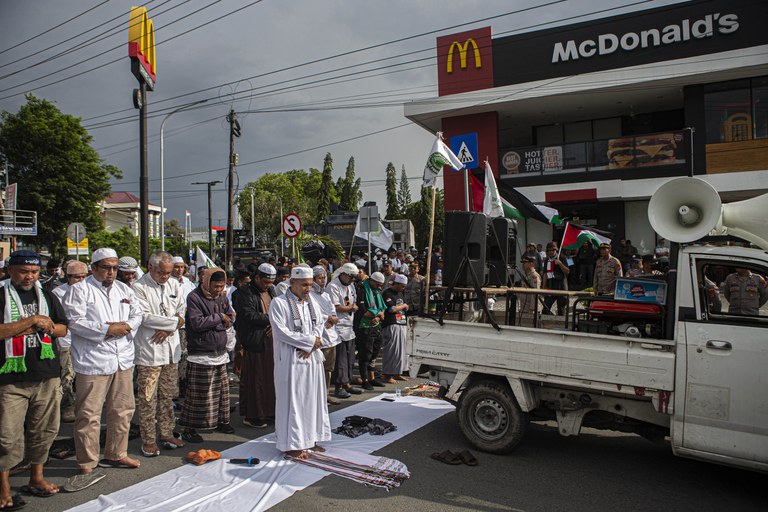 Pengunjuk rasa yang tergabung dalam Umat Muslim Sulawesi Tengah melakukan salat Jumat di tengah aksi demonstrasi bela Palestina di depan gerai McDonald’s yang diboikot selama seminggu di Kota Palu, Sulawesi Tengah, 3 November 2023, sebagai respons atas berita bahwa McDonald's di Israel memberikan makanan gratis bagi tentara Israel dalam perang melawan Hamas. McDonald's Indonesia dalam pernyataannya menegaskan bahwa gerainya di Indonesia adalah milik pengusaha lokal yang mempekerjakan lebih dari 16.000 pekerja Indonesia dan independen dari McDonald's di negara lain termasuk McDonald's Israel. [Taufan Bustan/BenarNews]