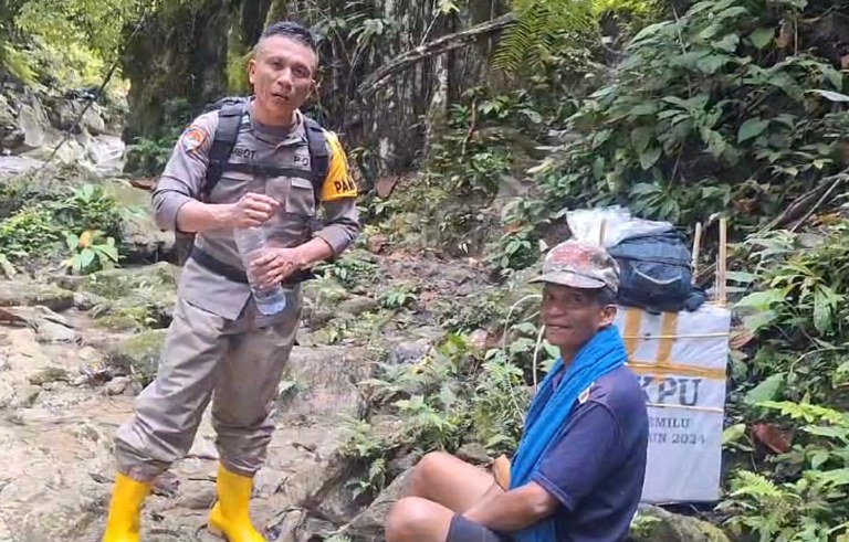 Anggota Polri, Aiptu Frets Adolof Rombot (kiri) didampingi warga beristirahat setelah melintasi sungai saat membawa logistik pemilu menuju TPS terpencil di Desa Baloa Doda, Kecamatan Pagimana, Kabupaten Banggai, Sulawesi Tengah, 9 Februari 2024. [Agus Tongkasi/BenarNews]