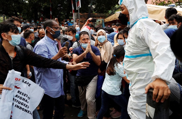Para pengunjuk rasa, pengungsi Afghanistan, berbicara dengan seorang petugas polisi, yang mengenakan alat pelindung diri (APD) di tengah pandemi COVID-19, dalam demonstrasi di luar gedung kantor perwakilan UNHCR di Jakarta, Selasa, 24 Agustus 2021. [Reuters]