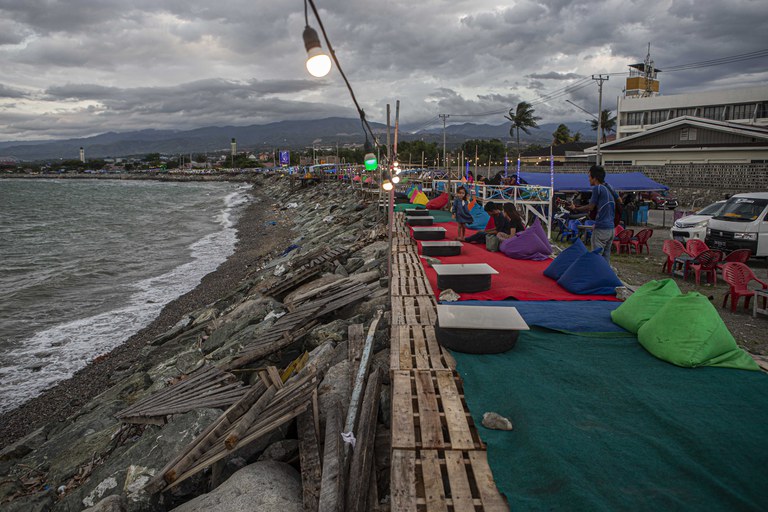 Seorang pengamen menghibur pengunjung yang datang bersantai di kafe milik penyintas gempabumi dan tsunami yang dibangun di atas tanggul Teluk Palu di pantai talise, Palu, Sulawesi Tengah, Rabu, 15 Februari 2023. Kafe sepanjang Pantai Talise dihias sedemikian rupa demi menarik pengunjung untuk datang. Beberapa asesoris yang dipasang seperti bantal duduk, karpet, dan lampu semuanya berwarna-warni. Asesoris ini menjadi salah satu daya tarik yang berhasil mendatangkan pengunjung selain pesona pantai yang indah. [Taufan Bustan/BenarNews]