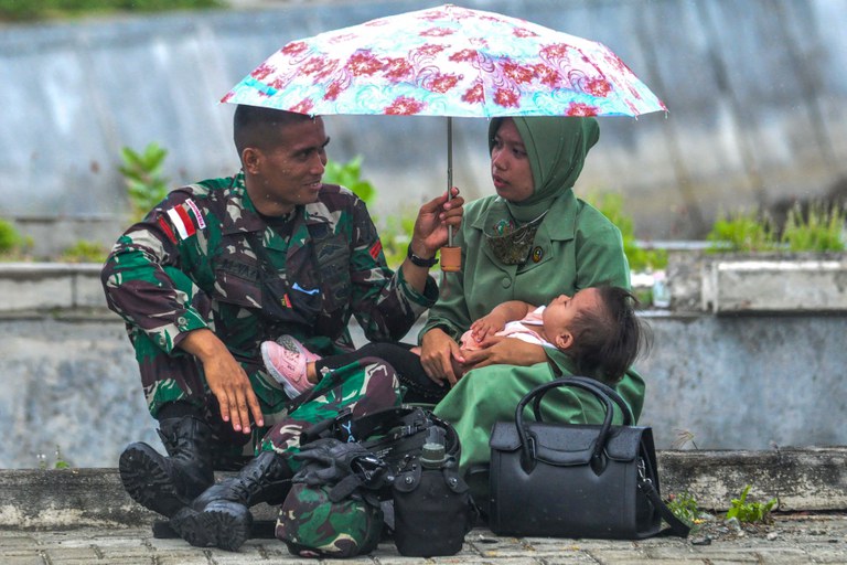 Seorang tentara Indonesia memegang payung untuk istri dan anaknya sebelum upacara pelepasan anggota TNI ke Papua, di pangkalan TNI Angkatan Laut di Palu, Sulawesi Tengah, pada 9 November 2021. [Muhammad Rifki/AFP]