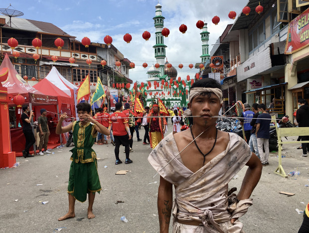 Salah satu Tatung peserta pawai memperlihatkan kekebalan tubuhnya yang ditusuk benda-benda tajam saat berjalan melewati salah satu jalan utama di Singkawang dengan latar belakang Masjid Raya Singkawang. (Ismira Lutfia Tisnadibrata/BenarNews)