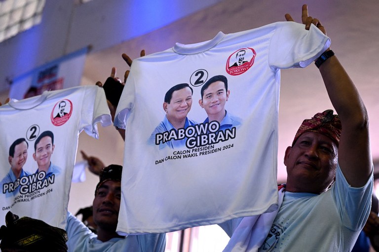 Pendukung capres Prabowo Subianto dan cawapres Gibran Rakabuming Raka mengacungkan kaos bergambar pasangan tersebut dalam kampanye di Denpasar, Bali, 9 Januari 2024. [Sonny Tumbelaka/AFP]