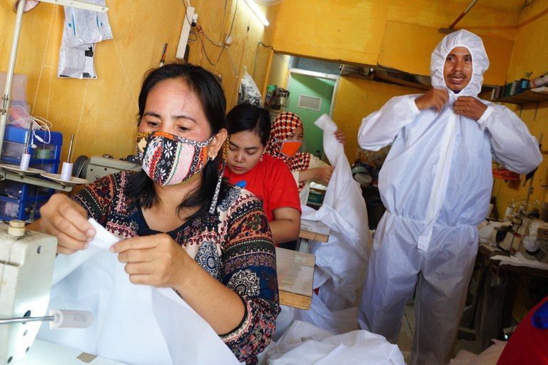 Sejumlah karyawan (kiri) memproduksi pakaian pelindung dari  virus corona COVID-19, sementara seorang pria (kanan) mengenakan pakaian tersebut di sebuah industri kecil di Tangerang, Banten, 2 April 2020. [Fajrin Raharjo/AFP]