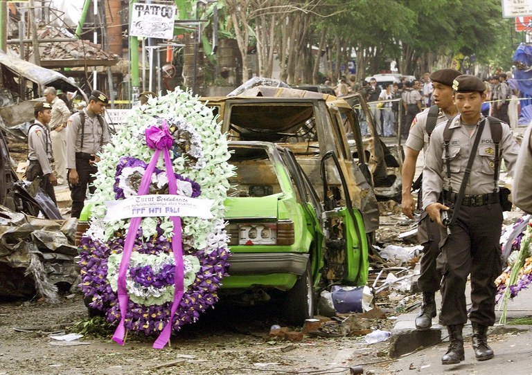 Polisi berjalan melewati karangan bunga di lokasi ledakan bom Bali di Pantai Kuta, yang menewaskan 202 orang, dua hari setelah serangan, 14 Oktober 2002. [Luis D'Orey/Reuters]