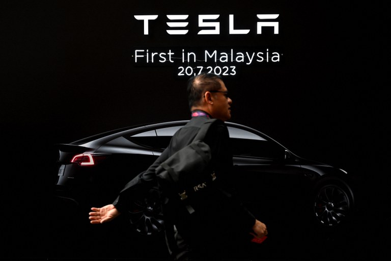 Seorang lelaki berjalan di depan kain rentang Tesla semasa pelancaran sulung kereta elektrik firma itu di Malaysia di Kuala Lumpur, 20 Julai 2023. [Mohd Rasfan/AFP]